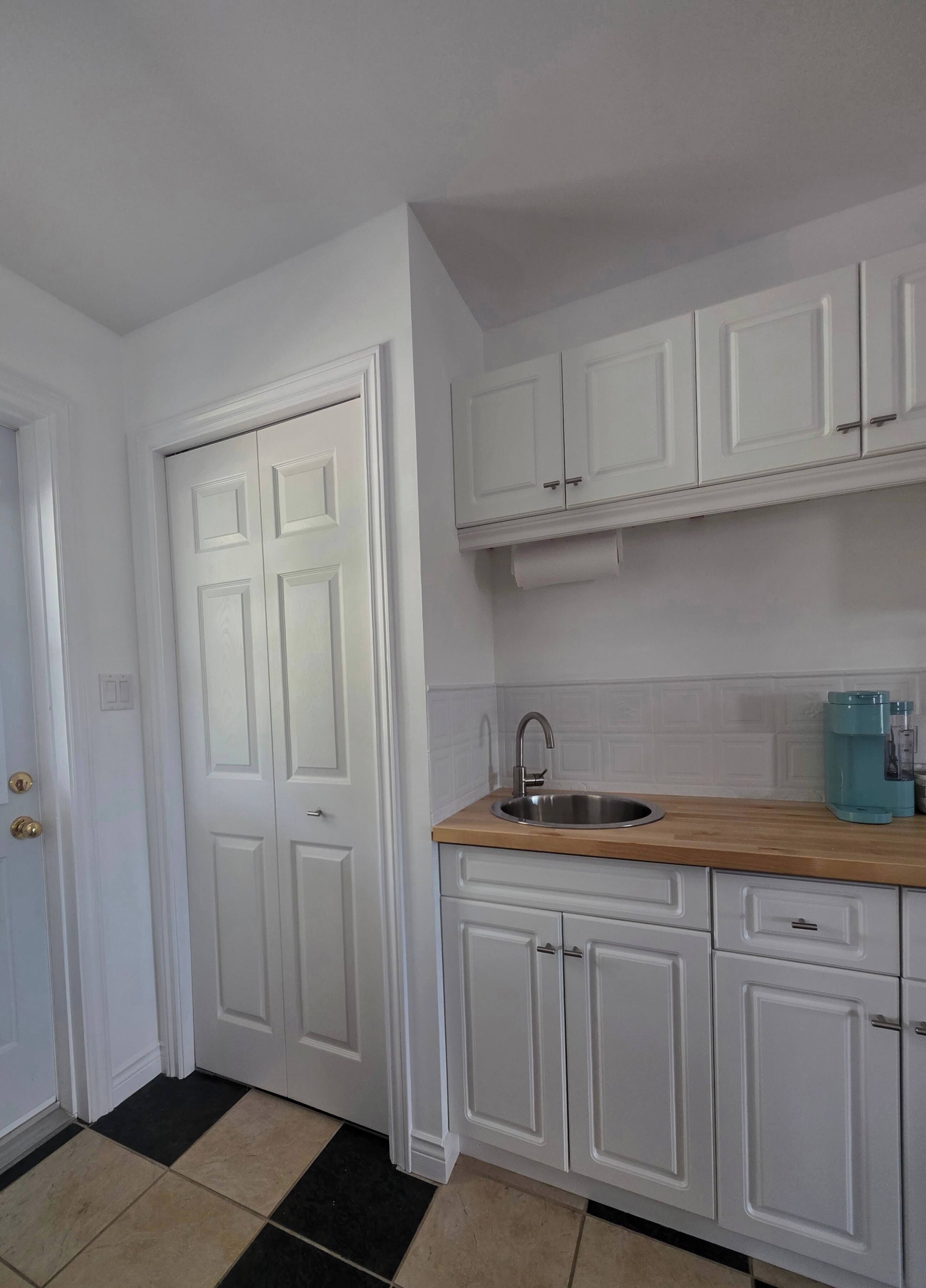 Una cocina con armarios blancos, un lavamanos de acero inoxidable y una encimera de madera.