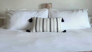 A bed with white bedding, a striped pillow, and a large landscape painting above. - Hunts Point Beachside Suite #11 (Hunts Point)