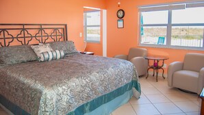 A bedroom with a large bed, a chair, a small table, and a window with a view.