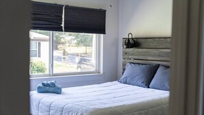 Een slaapkamer met een bed, een raam met jaloezieën, een hoofdeinde en een waterkoker aan de muur.