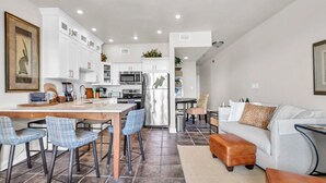 A modern kitchen with white cabinets, a stainless steel refrigerator, and a dining area with a wooden table and blue chairs.