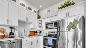 A modern kitchen with white cabinets, stainless steel appliances, and a tiled floor.