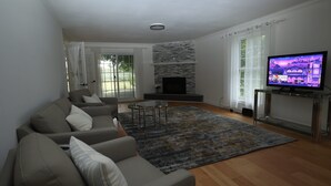 Una sala de estar moderna con un sofá, chimenea, televisor y vistas amplias a través de grandes ventanales.