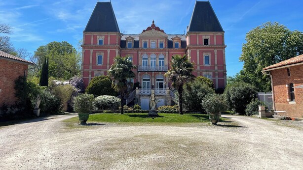 A large, symmetrical building with two prominent towers, a central entrance with a balcony, and a well-maintained garden in front.