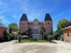 Un edifici gran i simètric, amb dues torres destacades, una entrada central amb balcó i un jardí ben cuidat al davant.