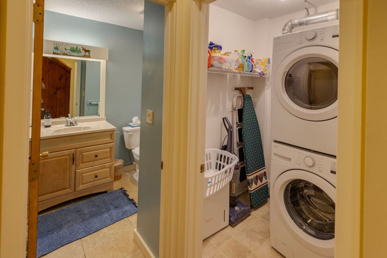A laundry area with a washing machine and dryer, a sink with a mirror, and a shelf with cleaning supplies.