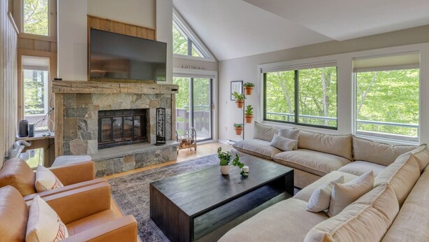 A spacious living room with a stone fireplace, large windows, a sofa set, and a coffee table.