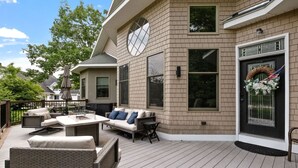 A modern house with a deck featuring outdoor furniture, large windows, and a decorative wreath on the front door. - Stunning Custom Home w/ Views (Lincoln)