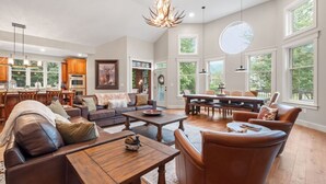 A spacious living room with a fireplace, a dining area, and large windows offering views of the outdoors. - Stunning Custom Home w/ Views (Lincoln)