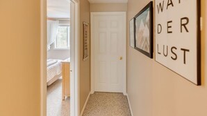 Un pasillo con una puerta blanca, paredes color beige y piso alfombrado. Hay cuadros en la pared y un cartel que dice "WANDER LUST".