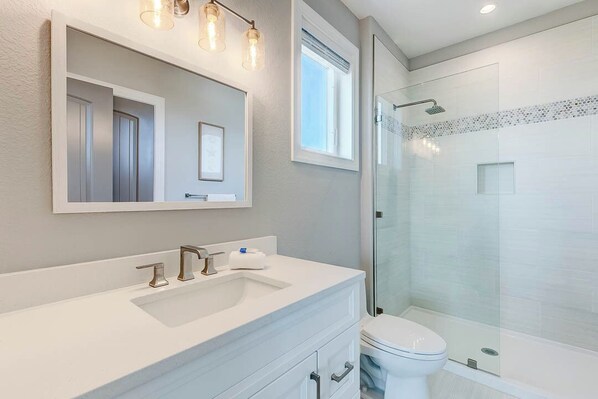 Une salle de bain moderne avec un grand miroir, un lavabo, des toilettes et une douche à parois de verre.