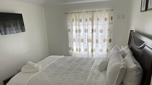 Una cama bien hecha con sábanas blancas, cabecera de madera y una ventana con cortinas florales.