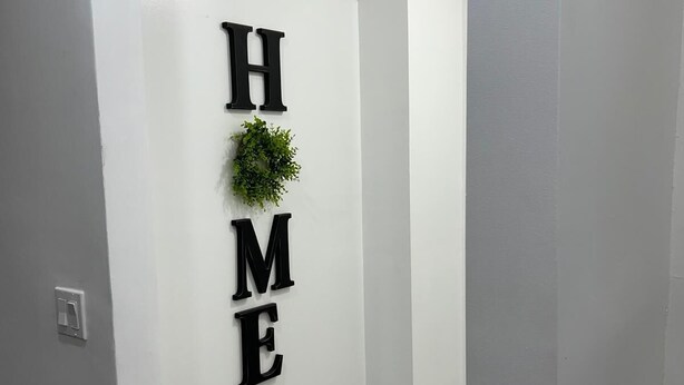 Un pasillo con una pared blanca que muestra la palabra “HOME” en letras negras y una guirnalda verde.