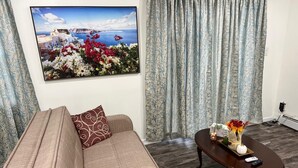 Una sala de estar con un sofá color beige, cojines estampados, una mesa de centro de madera con un jarrón de flores y un cuadro de una escena costera.