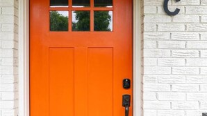 Una puerta naranja brillante con una ventana, un sistema de cierre por teclado y una letra 'C' en la pared.