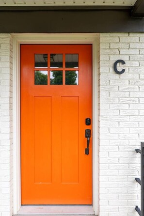 Una puerta naranja brillante con una ventana, un sistema de cierre por teclado y una letra 'C' en la pared.