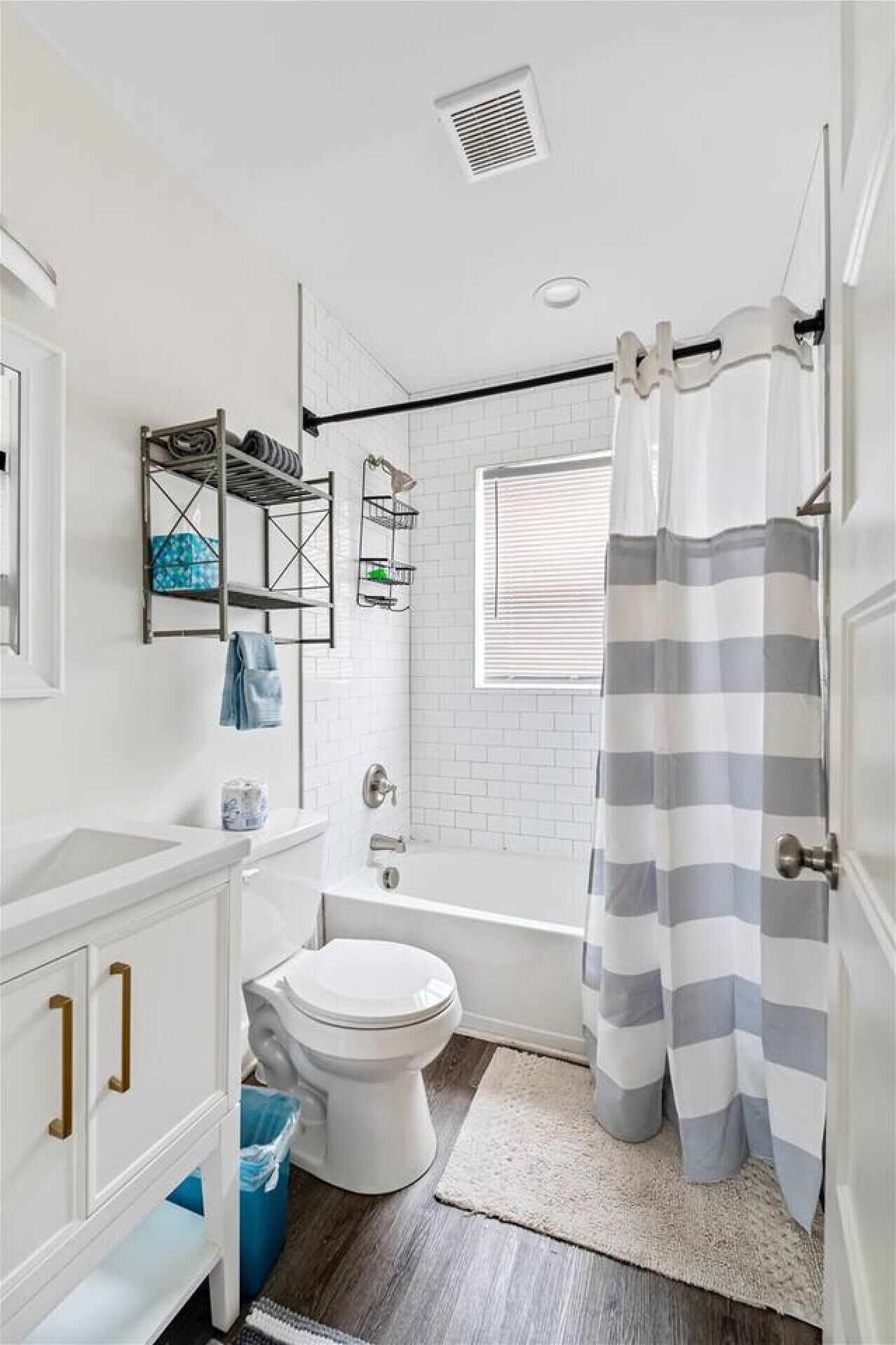 A bathroom with a white toilet, a bathtub, a shower curtain, a towel rack, and a window with blinds.