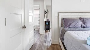 Un dormitorio con cama, una puerta blanca y un pasillo que conduce a un baño.