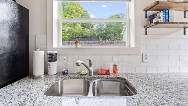 Una cocina con un lavamanos doble, una ventana con vistas a árboles y un estante con libros y objetos decorativos.