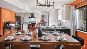 Un espace repas moderne avec une table en bois dressée pour six personnes, un vase décoratif et une cuisine en arrière-plan.