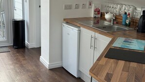 A compact kitchen with a dishwasher, a sink, and a countertop with a fire blanket and various kitchen items. - Modern Split-Level 2-Bed Apartment with Balcony (Causeway Coast and Glens)