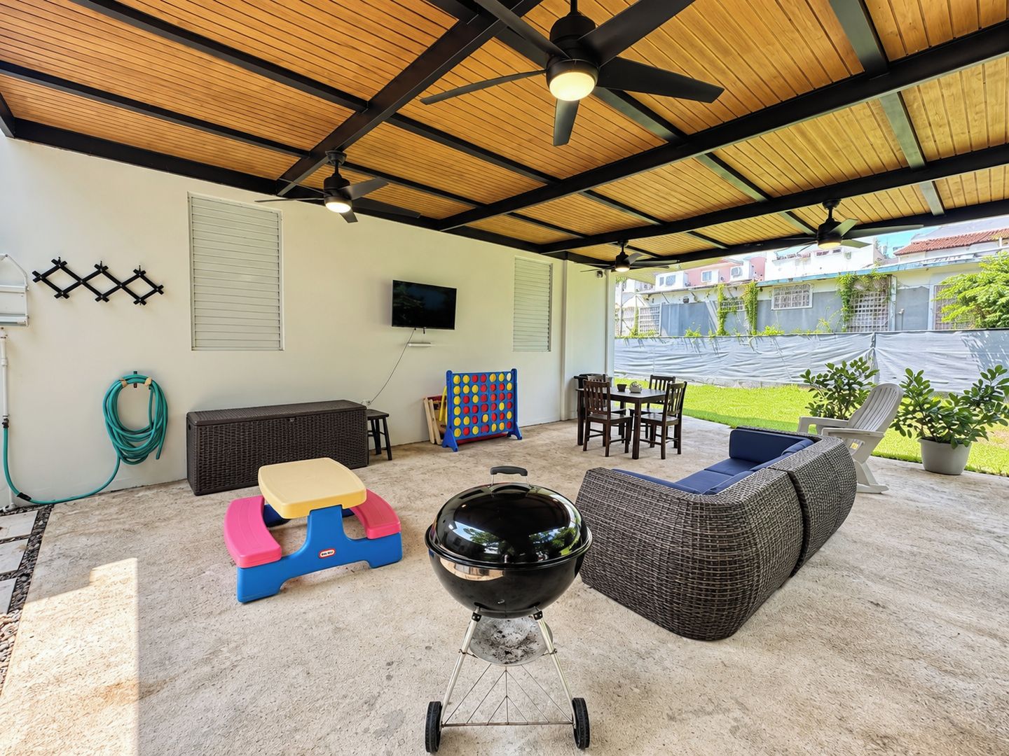 Un patio techado al aire libre con ventilador de techo, una parrilla, una zona de estar y un televisor montado en la pared.