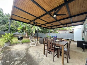 A covered patio area with a table and chairs, a grill, and potted plants.