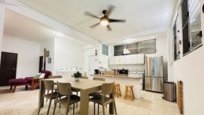A modern kitchen with a dining area, featuring a central island, stainless steel appliances, and a ceiling fan.
