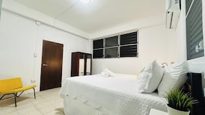A bedroom with a bed, a chair, a wardrobe, a window, and a potted plant.