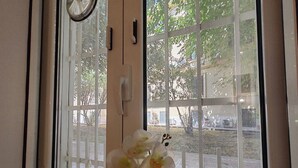 Une fenêtre donnant sur un espace extérieur clôturé, une porte avec une poignée et une horloge au mur.