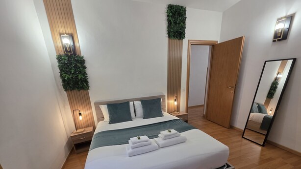 Une chambre moderne avec un grand lit, un plancher en bois, une table de chevet avec une lampe, un miroir et une porte.