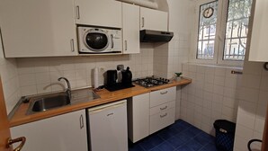 Une cuisine compacte avec des meubles blancs, un four à micro-ondes, une cuisinière à gaz, un évier et un petit réfrigérateur.