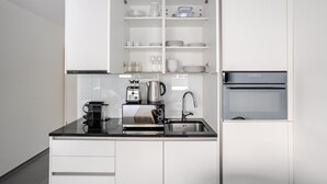 A modern kitchen with white cabinets, a black countertop, a coffee machine, a toaster, a kettle, and a built-in oven. - Blueground | Basel-Iselin, view, nr Rhine (Basel)