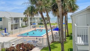 A hotel with a swimming pool surrounded by palm trees and a view of the ocean.