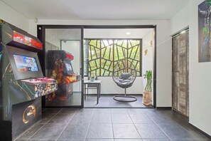 A room with a gaming console, a hanging chair, a potted plant, and a view through a glass door.