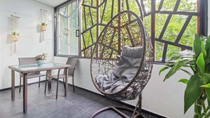 A room with a glass table, wicker chairs, a hanging chair, and a large window with a view of greenery. - 6 Bedoom Apartment with Balcony, Pool tableJacuzzi (Medellín)