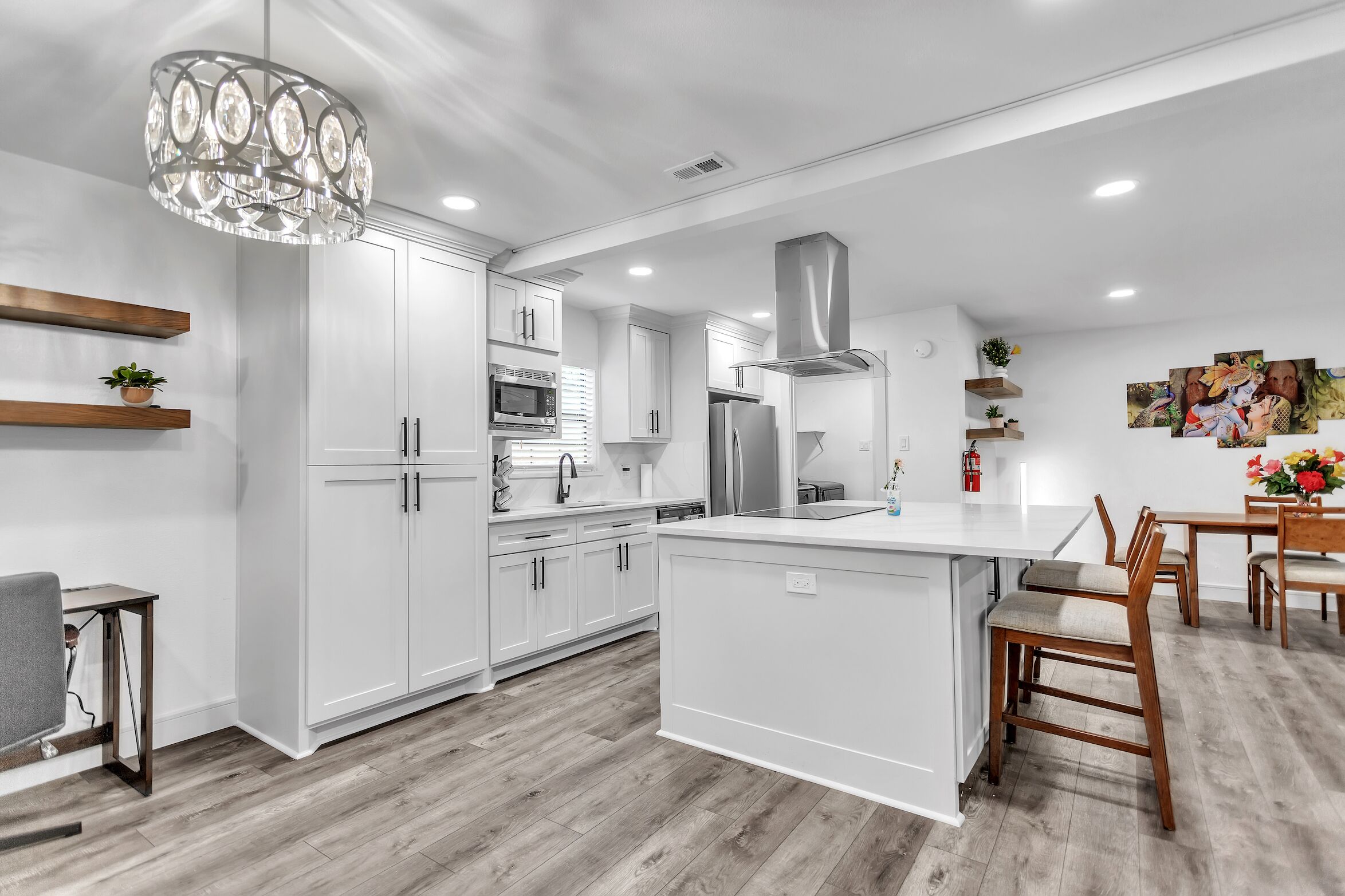 A modern kitchen with white cabinetry, a central island, and a dining area with wooden chairs.