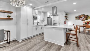 Una cocina moderna con armarios blancos, una isla central y un comedor con sillas de madera.