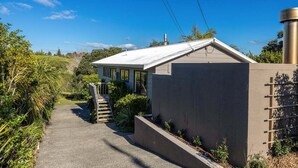 A modern house with a concrete exterior, a sloped roof, and a pathway leading to the entrance. - Villetta Hauraki by Waiheke Pure - Spacious modern home, walk to Palm Beach (Waiheke Island)