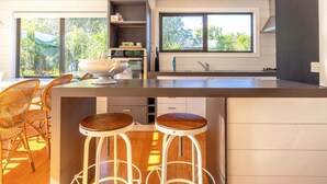 A modern kitchen with a large island, bar stools, and a view of greenery outside. - Villetta Hauraki by Waiheke Pure - Spacious modern home, walk to Palm Beach (Waiheke Island)