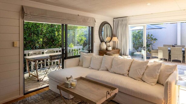 A spacious living room with a large sofa, a wooden coffee table, and a view of an outdoor patio area. - Villetta Hauraki by Waiheke Pure - Spacious modern home, walk to Palm Beach (Waiheke Island)