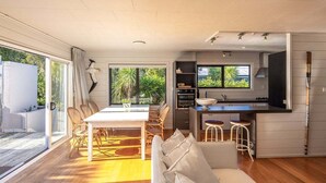A modern kitchen with a dining area, large windows, and a wooden deck. - Villetta Hauraki by Waiheke Pure - Spacious modern home, walk to Palm Beach (Waiheke Island)