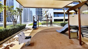 Une aire de jeux pour enfants avec un toboggan, des structures d’escalade et un espace pour les poussettes.