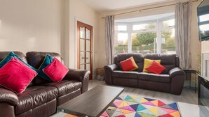 A living room with two leather sofas, colorful cushions, a glass coffee table, and a geometric rug. - Two bedroom house with free parking, near city centre, sleeps up to five (Edinburgh)
