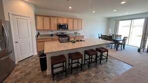 A modern kitchen with granite countertops, wooden cabinets, and a central island with bar stools. - 4-bedroom house in wonderful Perris with WiFi, AC (Perris)
