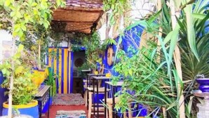 A narrow pathway leading to a seating area with blue and yellow planters, a thatched roof, and a colorful rug. - Authentic Riad in Marrakech - A Living Museum of Moroccan Art (Marrakech)