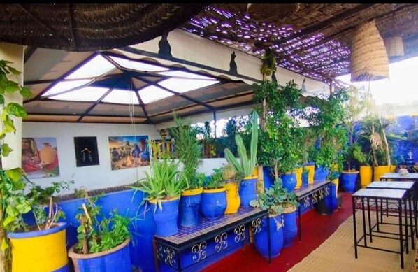 A restaurant with a covered outdoor seating area, featuring blue and yellow planters with various plants, a red carpet, and a decorative ceiling. - Authentic Riad in Marrakech - A Living Museum of Moroccan Art (Marrakech)