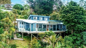 Una casa moderna con fachada de vidrio, elevada sobre pilotes, rodeada de exuberante vegetación.