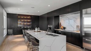 A modern kitchen with a marble island, bar stools, a built-in wine rack, and a large refrigerator.