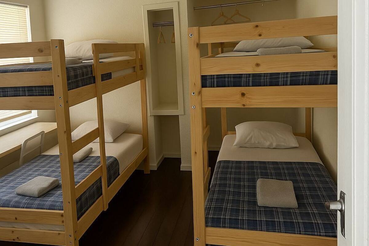 A room with three bunk beds, wooden flooring, a window with blinds, and a door.